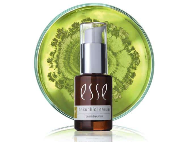 A brown bottle with a white pump, labeled "esse bakuchiol serum," is placed in front of a transparent green round disk with an intricate design, and a white background.